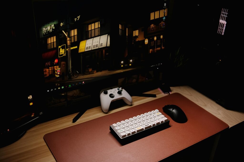 Close-up of a gaming desk setup featuring a keyboard, controller, and monitor at night.